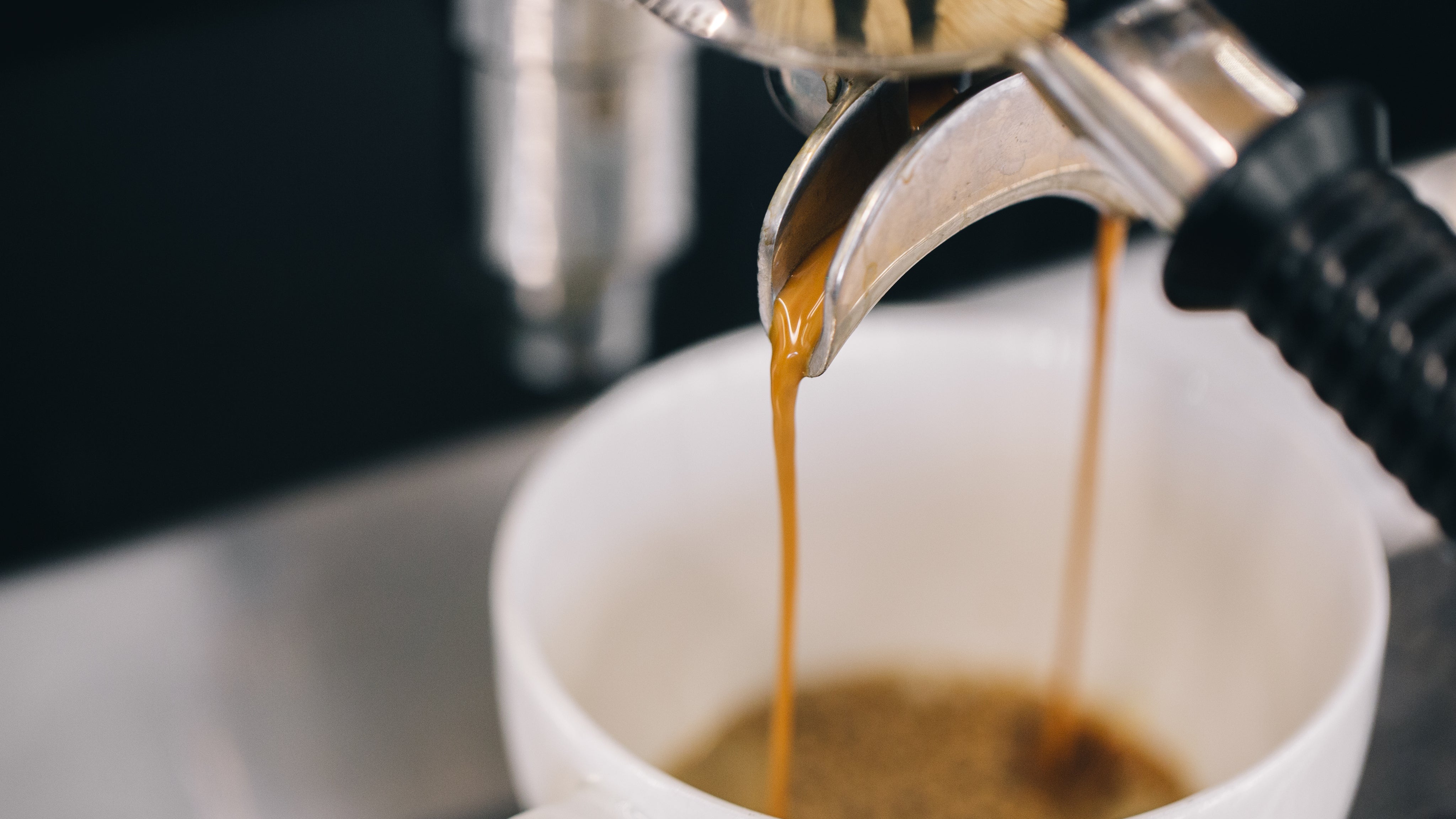 Espresso being poured from a machine into a white cup.